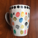 White mug with colorful dot patterns on a wooden surface