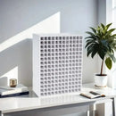 White grid-like organizer on a desk with books and a plant in a bright room.