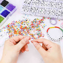 Hands working with colorful beads and letter beads on a light surface.