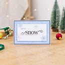 Christmas card with 'Let It Snow' text on a festive background with decorations.