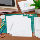 Crafting materials on a table including paper, scissors, and a cutting mat.