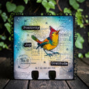 Decorative card with a colorful bird illustration and motivational words on a wooden surface with greenery in the background.