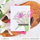 Card with floral design and message on a wooden surface with flowers and a pen.