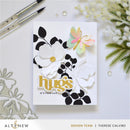 Card with floral design and 'hugs it's your day' text, surrounded by crafting tools and flowers on a light background.