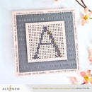 Cross-stitched letter 'A' on a grid with text background, featuring the brand 'Altenew'.