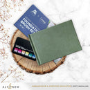 Green notebook on a wooden stump with art supplies and branding elements.