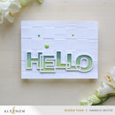 Card with 'HELLO' cutout design on a wooden surface with flowers