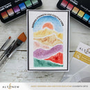 Colorful watercolor card with mountain design and 'Sending Strength and Positive Vibes' text, surrounded by art supplies on a wooden surface.
