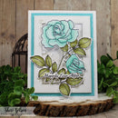Card with turquoise roses and 'Happily Ever After' text on a wooden surface with greenery.