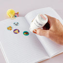 Hand using a Hero Arts Sticker Stamper on a notebook with animal-themed stickers.