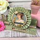 Decorative birthday card with vintage-style illustration of a woman holding a glass of champagne, surrounded by flowers and a potted plant.