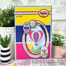 Colorful greeting card with hot air balloon design and text, placed on a surface with plants.