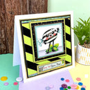 Colorful greeting card with a cartoon character on a wooden surface with buttons and a plant.