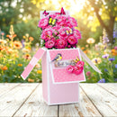 Pink gift box with flowers and decorative elements on a wooden surface with a garden background