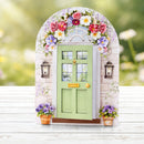 Decorative fairy door with floral arch and potted plants on a wooden surface.