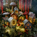 Miniature fairy village with lit houses and mushroom-like structures against a dark background.