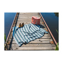 Blue and white striped towel on a wooden dock with a red bag and shoes.