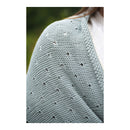 Close-up of a person wearing a light blue knitted shawl with a blurred green background