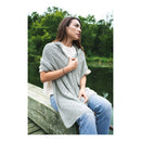 Woman sitting on a wooden bench by a lake, wearing a light gray poncho.