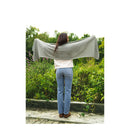 Person standing outdoors with a gray shawl draped over their shoulders, surrounded by greenery.