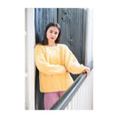Woman wearing a yellow sweater leaning against a wooden door.
