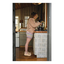 Person standing in a kitchen filling a kettle with water wearing knitted brunch shorts and brown jumper