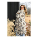 Woman wrapped in a large, patterned blanket outdoors.