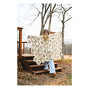 Person standing on a wooden deck holding a large, patterned blanket