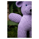 Crocheted purple teddy bear on a green background