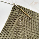 Crocheted fabric with a gold crochet hook on a light background