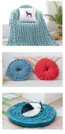 Collection of knitted products including a blanket, cushions, and a mat on a white background.
