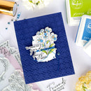 Blue card with floral design and text on a white surface with craft supplies.