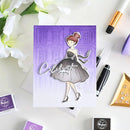Purple card with a design of a woman in a dress and the word 'Celebrate' on a white surface with flowers and stationery items.