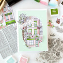 Card with decorative building design and floral elements on a table with stamping tools.