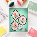 Card with floral designs and text on a white surface with makeup brushes.