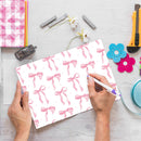 Person holding a pen over a sheet of paper with pink bow pattern on a desk with stationery items.