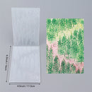 Two sheets of paper with different designs, one with a forest pattern and the other plain, on a gray background.