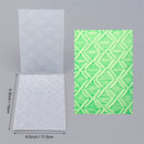 Two textured paper sheets, one white and one green with a geometric pattern, on a gray background.
