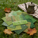 Collection of green fabric swatches with a teapot on a checkered cloth in an outdoor setting.