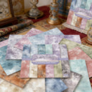 Collection of Aether Scrapbooking Paper Sheets on a textured surface with decorative items in the background.