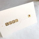 White card with 'LOVE' spelled out using gold letter stamps on a white background