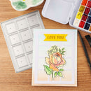 Card with a rose design and 'LOVE YOU' text on a wooden surface with art supplies.