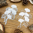 White leaf-shaped cutouts on a wooden surface with pine cones.