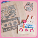 Metal cutting dies shaped like a cake, fork, and rabbit with 'Happy Birthday' text on a pink background.