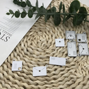 Decorative metal charms shaped like envelopes on a textured surface with green leaves.