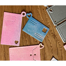 Metal die cut shapes on a wooden surface, including pink, blue, and gray hearts and rectangles.