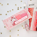 Pink birthday card with floral design and a small bottle on a white background with gold stars.
