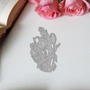 Metal floral bookmark on a white surface with pink roses and an open book in the background.