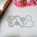 Metal cutout of 'We Love You' on a white surface with pink roses and an open book.
