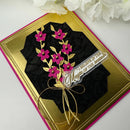 Decorative card with black fabric, pink flowers, gold ribbon, and 'I believe in the magic of the season' text on a white background.